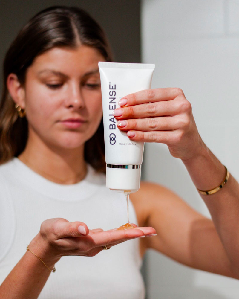 Woman Squeezing a Bottle of Balense Skincare